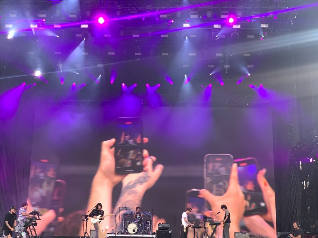 People holding up cell phones in backdrop of band playing. Osheaga 2023. Photo Rachel Levine