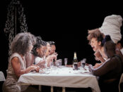 Laughing women at a dinner table in a theatre piece.