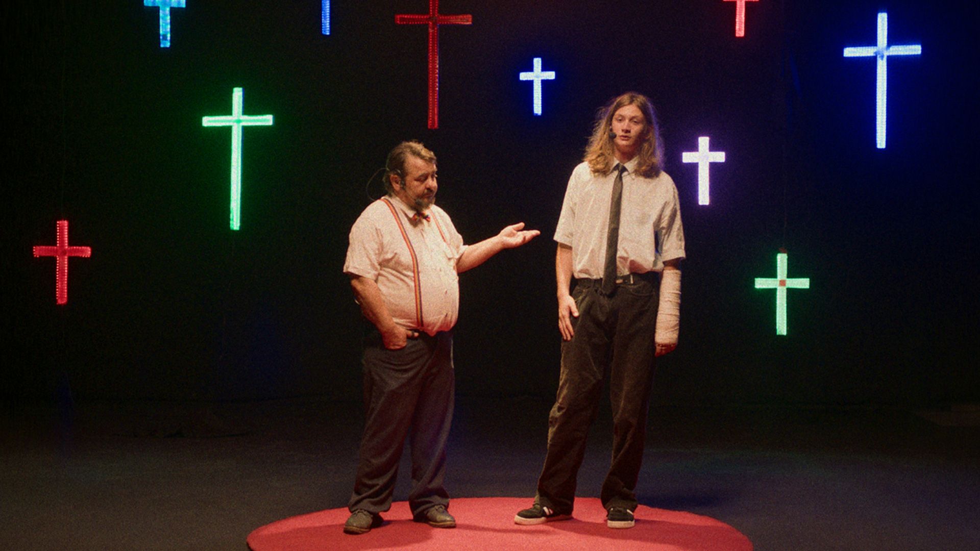 Two men surrounded by neon crosses