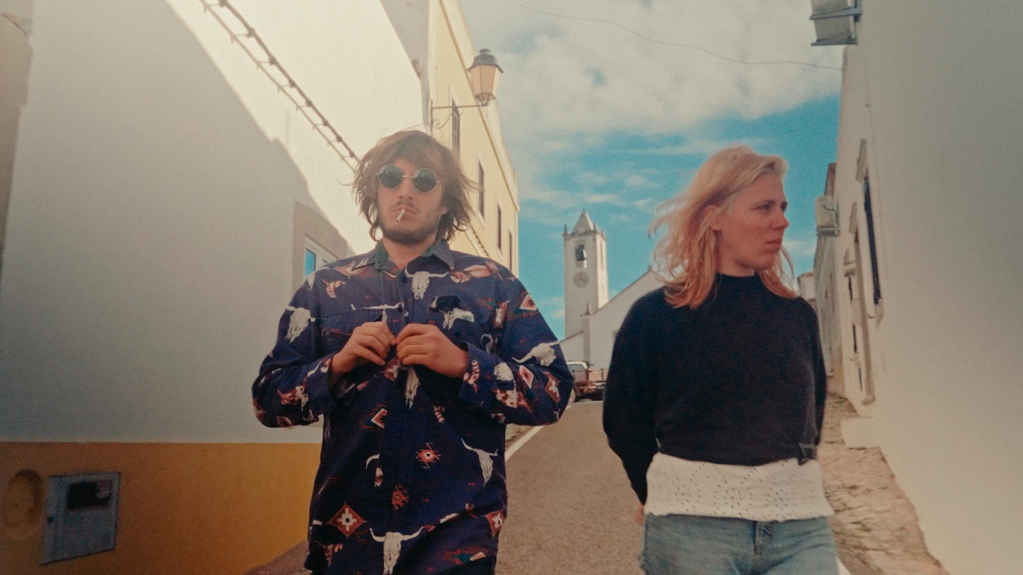 A man in a colorful button up shirt walks beside a woman in casual clothes.