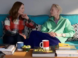 Julianne Moore and Tilda Swinton sit side by side on a blue couch